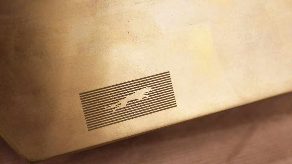 Jaguar leaper incorporated into fine horizontal stripes on a brass-colored surface.